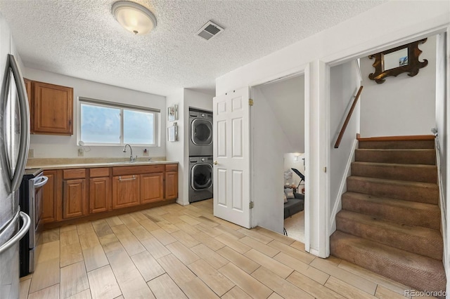 laundry area with a sink, wood tiled floor, laundry area, stacked washer / drying machine, and visible vents