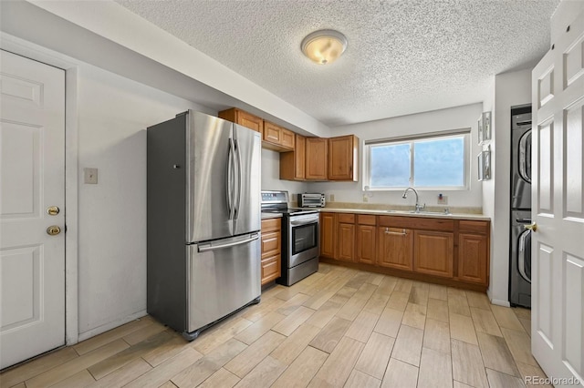 kitchen with a sink, brown cabinets, stainless steel appliances, wood finish floors, and stacked washer and dryer