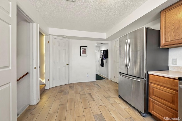 kitchen with light wood finished floors, light countertops, freestanding refrigerator, brown cabinetry, and a textured ceiling
