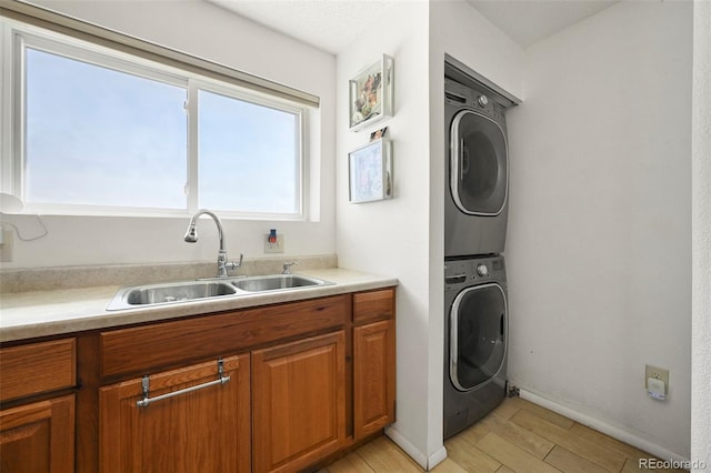 washroom with a sink, baseboards, light wood-style floors, stacked washer and clothes dryer, and laundry area