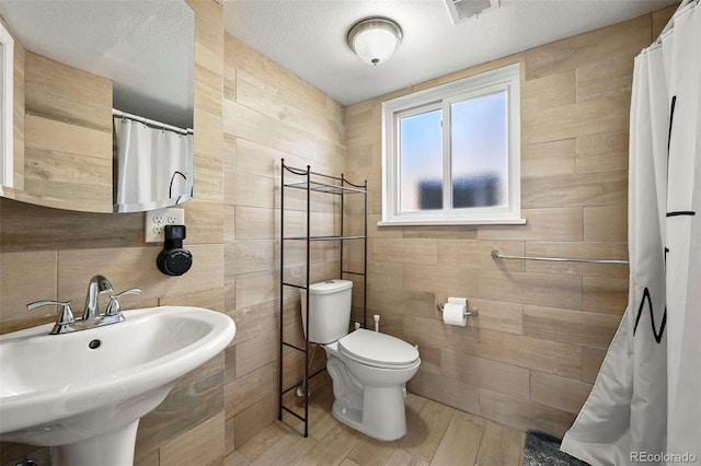 bathroom featuring a sink, toilet, tile walls, visible vents, and wood finished floors