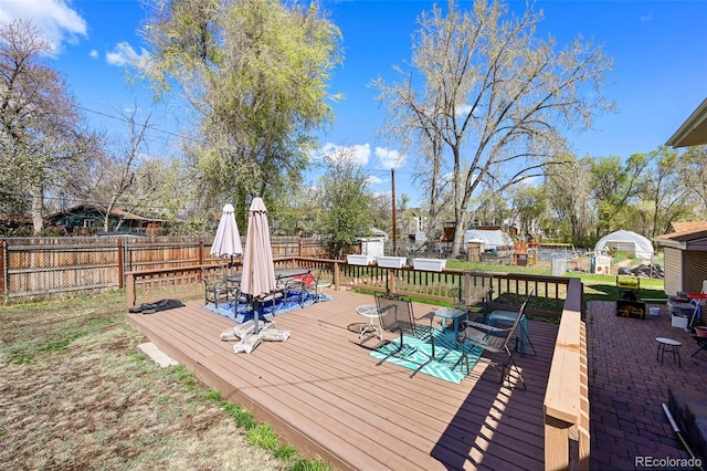 wooden terrace with a storage unit, an outbuilding, outdoor dining area, and a fenced backyard