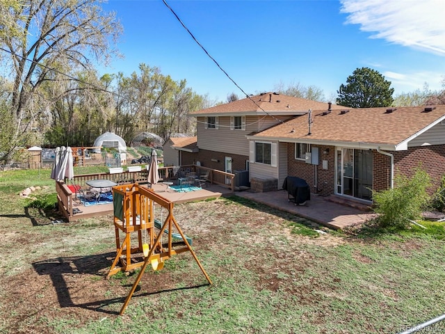 rear view of house with fence, a shingled roof, a wooden deck, a patio, and brick siding