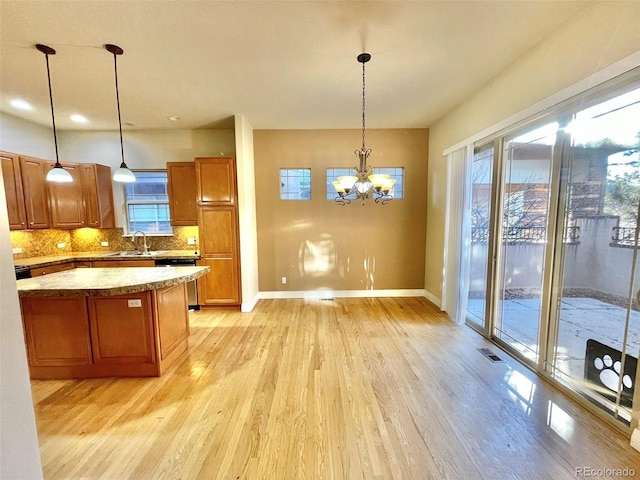 kitchen featuring pendant lighting, stainless steel dishwasher, decorative backsplash, a notable chandelier, and light hardwood / wood-style floors