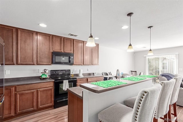 kitchen featuring a breakfast bar area, brown cabinetry, visible vents, light wood-style flooring, and black appliances