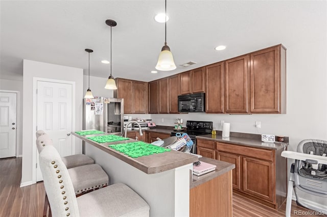 kitchen featuring a kitchen bar, light wood finished floors, black appliances, and visible vents