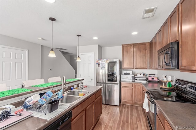 kitchen with visible vents, brown cabinets, light wood-type flooring, black appliances, and a sink