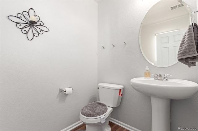 half bath featuring a sink, baseboards, toilet, and wood finished floors