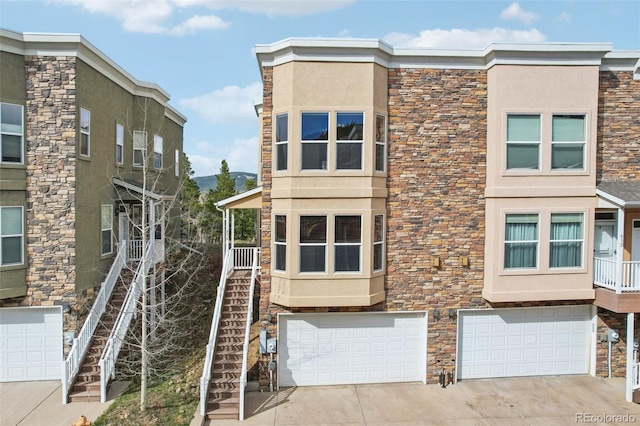view of side of property featuring driveway, a garage, stairs, stone siding, and stucco siding