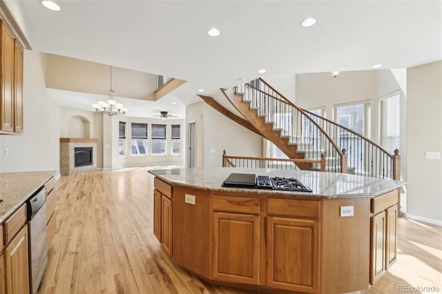 kitchen featuring black gas cooktop, light wood-style flooring, a tile fireplace, stainless steel dishwasher, and a kitchen island