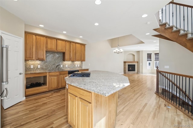 kitchen featuring light stone countertops, light wood finished floors, open floor plan, tasteful backsplash, and a kitchen island