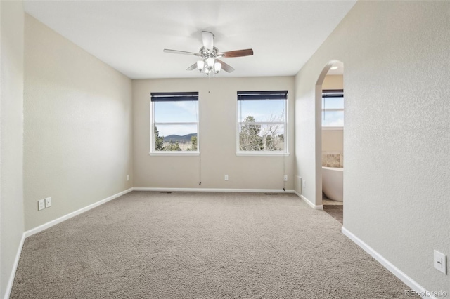 unfurnished room featuring carpet flooring, arched walkways, ceiling fan, and plenty of natural light
