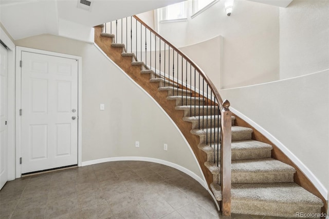 stairs with baseboards, visible vents, tile patterned floors, and lofted ceiling
