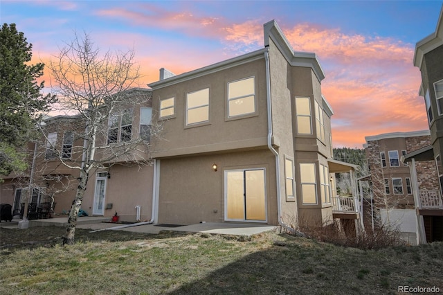 back of house at dusk with a lawn, a patio area, and stucco siding