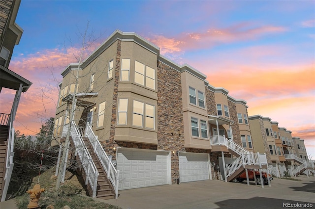 property at dusk with an attached garage, driveway, and stairway