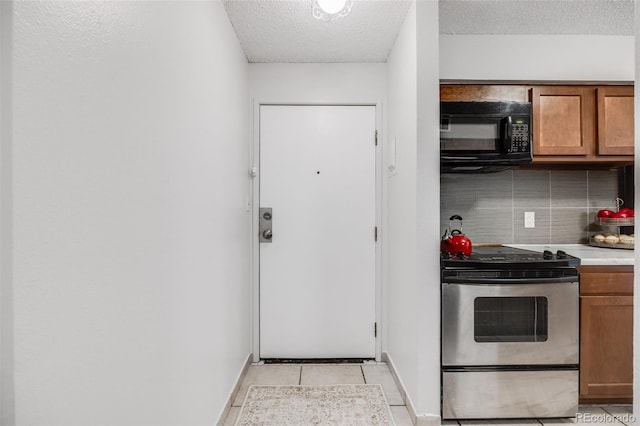 kitchen featuring stainless steel range with electric cooktop, black microwave, a textured ceiling, decorative backsplash, and brown cabinetry