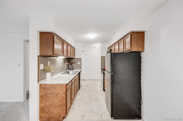 kitchen featuring freestanding refrigerator, a sink, light countertops, brown cabinets, and a textured ceiling