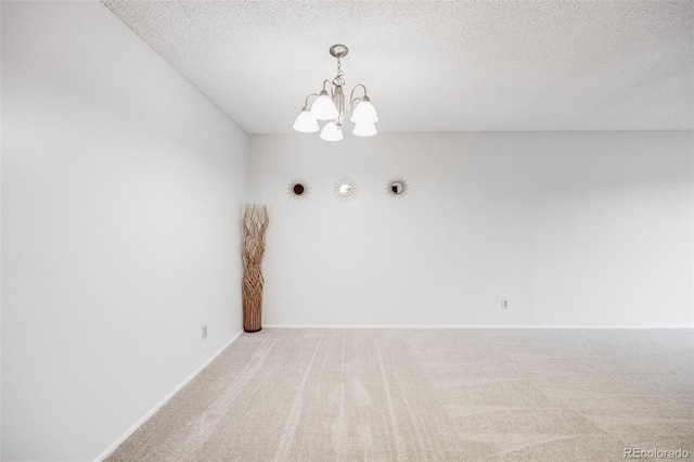spare room featuring carpet flooring, a chandelier, a textured ceiling, and baseboards