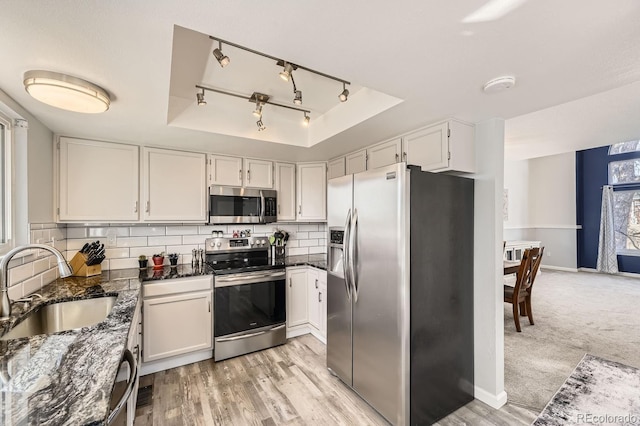 kitchen with sink, appliances with stainless steel finishes, white cabinetry, backsplash, and a tray ceiling