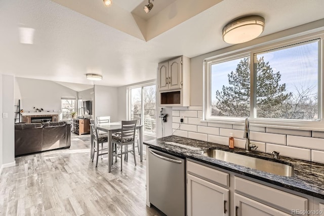 kitchen featuring sink, a brick fireplace, light hardwood / wood-style flooring, dishwasher, and decorative backsplash