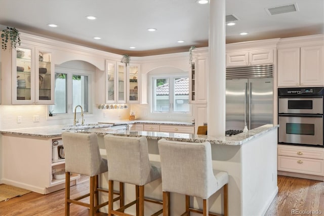 600 Vine St, Denver, CO 80206 - kitchen with appliances with stainless steel finishes, light stone counters, light wood-style floors, a breakfast bar, and glass insert cabinets