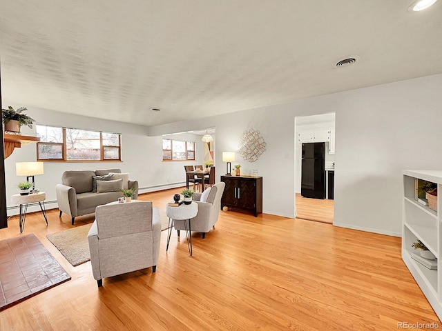 living room with a healthy amount of sunlight, a baseboard heating unit, and light hardwood / wood-style floors