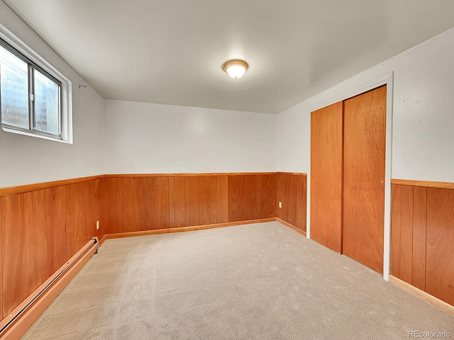 empty room featuring carpet flooring, wooden walls, and baseboard heating