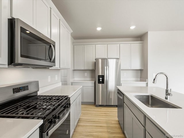 kitchen with stainless steel appliances, a sink, white cabinetry, light wood-style floors, and light countertops