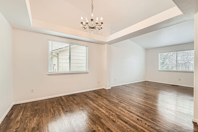 empty room featuring a notable chandelier, a tray ceiling, and dark wood-type flooring