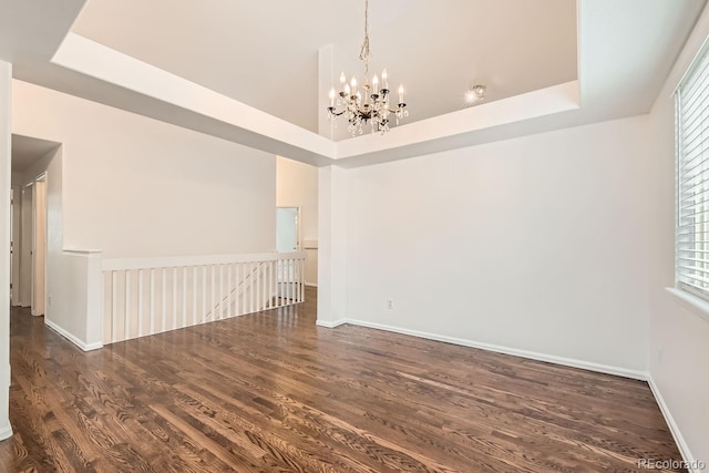 spare room with a wealth of natural light, a tray ceiling, dark hardwood / wood-style flooring, and a notable chandelier