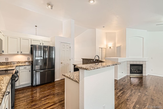 kitchen featuring an island with sink, white cabinets, stainless steel fridge, electric range, and light stone countertops