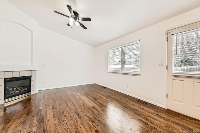 unfurnished living room with ceiling fan, dark hardwood / wood-style flooring, a tiled fireplace, and vaulted ceiling