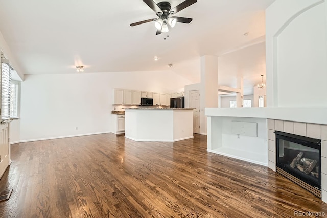 unfurnished living room featuring vaulted ceiling, dark hardwood / wood-style flooring, ceiling fan with notable chandelier, and a fireplace