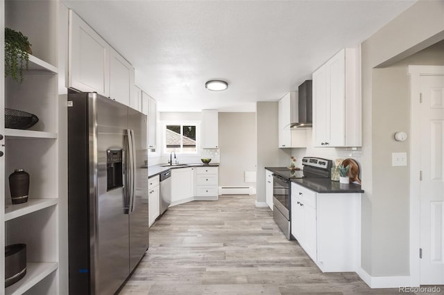 kitchen with appliances with stainless steel finishes, a baseboard radiator, sink, white cabinets, and wall chimney exhaust hood