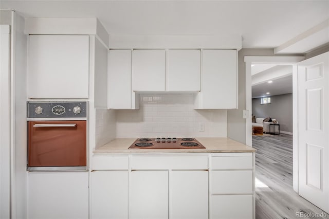 kitchen with stovetop, light hardwood / wood-style flooring, white cabinets, oven, and backsplash