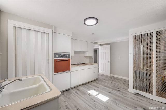 kitchen with sink, light hardwood / wood-style flooring, white cabinetry, wall oven, and tasteful backsplash