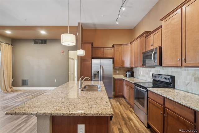 kitchen with decorative light fixtures, hardwood / wood-style floors, appliances with stainless steel finishes, and an island with sink