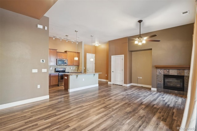 unfurnished living room featuring a tile fireplace, dark wood-type flooring, a high ceiling, and ceiling fan