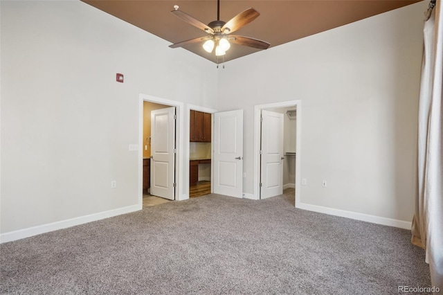 unfurnished bedroom with a spacious closet, a towering ceiling, a closet, ceiling fan, and light colored carpet