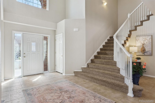 entryway with tile patterned flooring, stairway, a high ceiling, and baseboards