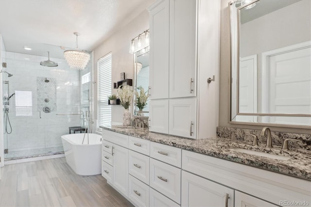 bathroom with double vanity, a chandelier, a shower stall, a freestanding bath, and a sink