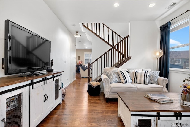 living area featuring a wealth of natural light, stairs, visible vents, and dark wood-type flooring