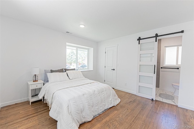 1486 S Kingston St, Aurora, CO 80012 - bedroom with a barn door, wood finished floors, baseboards, and ensuite bath