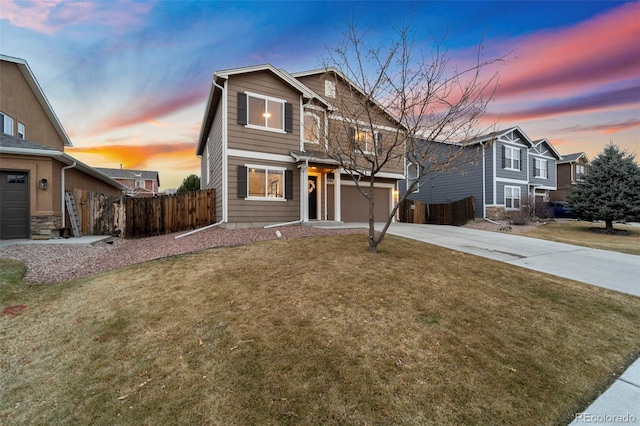 traditional-style home featuring a lawn, concrete driveway, an attached garage, and fence