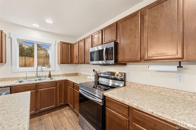 kitchen with light countertops, brown cabinets, wood finished floors, stainless steel appliances, and a sink