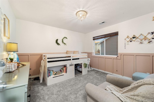 carpeted bedroom with visible vents, a textured ceiling, and wainscoting