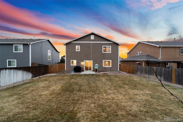 back of house at dusk with a lawn, a patio, and a fenced backyard