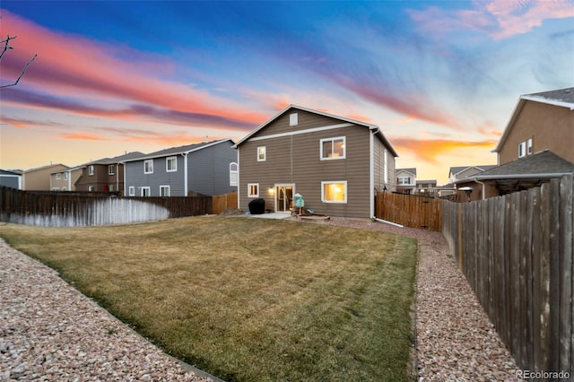 back of property at dusk featuring a patio, a yard, and a fenced backyard