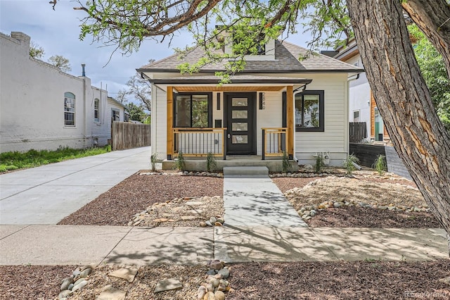 view of front of home with covered porch, fence, and a shingled roof