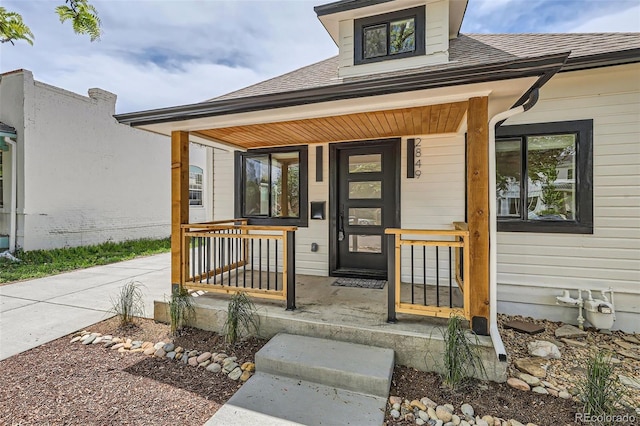 entrance to property with covered porch and roof with shingles